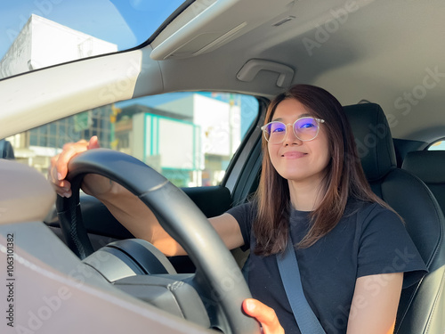 Front view of asian Thai woman driving a car with smiling face, hand holding steering wheel, car insurance and happy work travel concept.