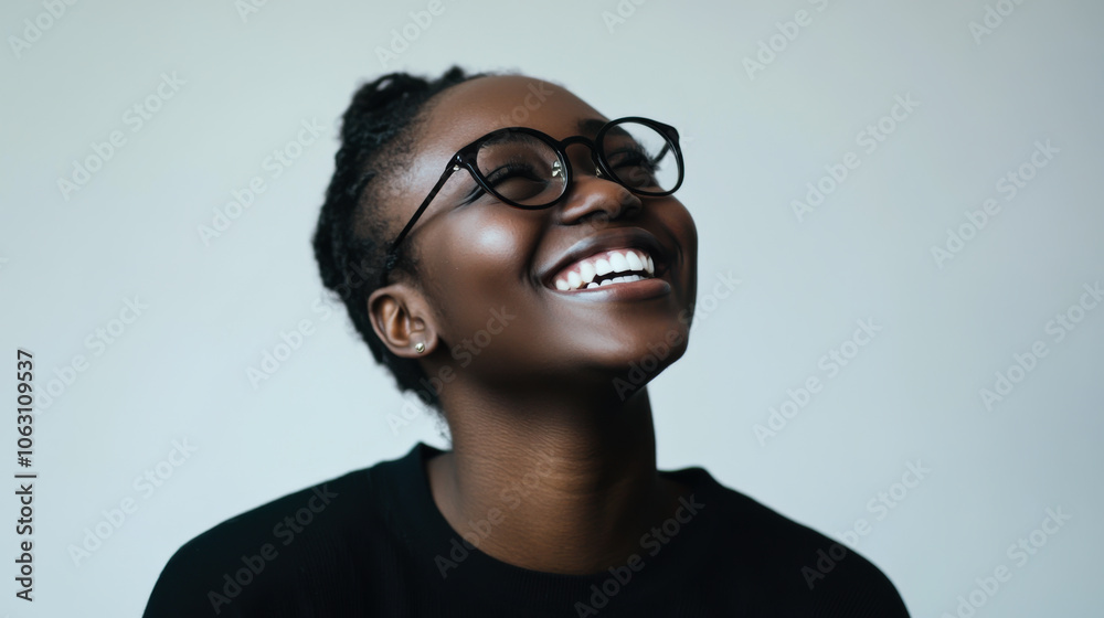 Fototapeta premium A young woman with glasses smiles warmly, showcasing joy and confidence against a soft light background in a candid indoor setting