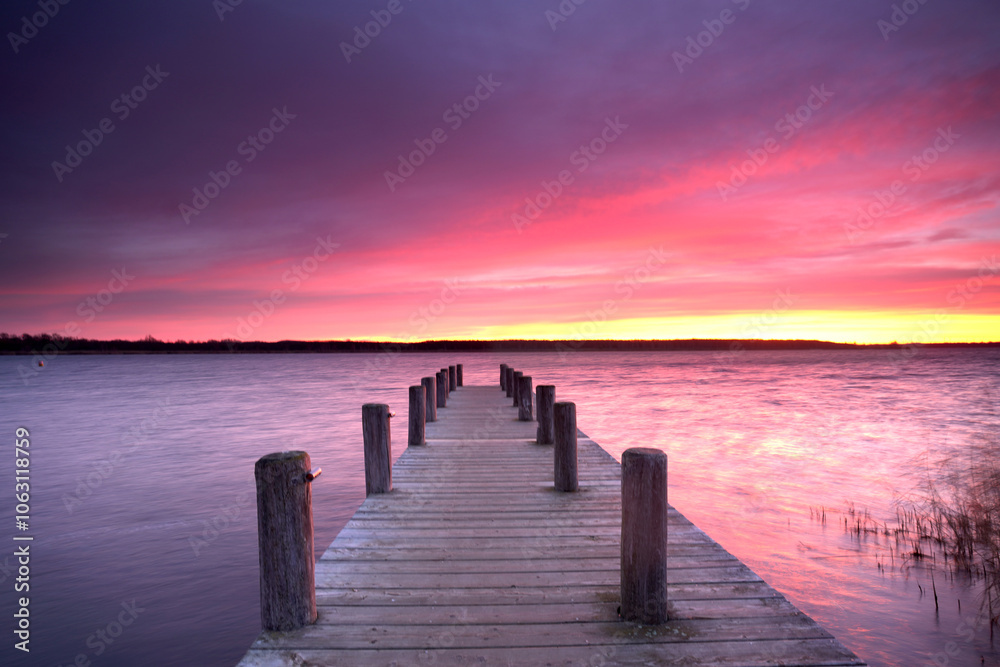 Obraz premium purple sunset light over a long wooden rustic pier at the lake