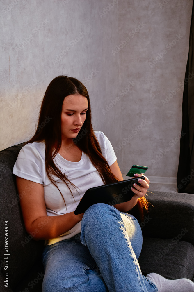  A happy young Hispanic woman holds a credit card and laptop, shopping online at home. A moment of digital shopping that highlights the convenience of modern purchases and using bonus money.