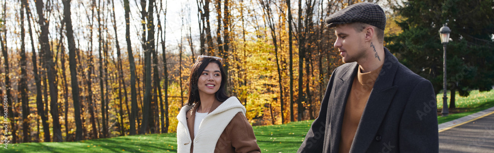 A couple dressed in warm autumn clothing walks hand in hand through vibrant fall landscapes. A couple dressed in warm autumn clothing walks hand in hand through vibrant fall landscapes.