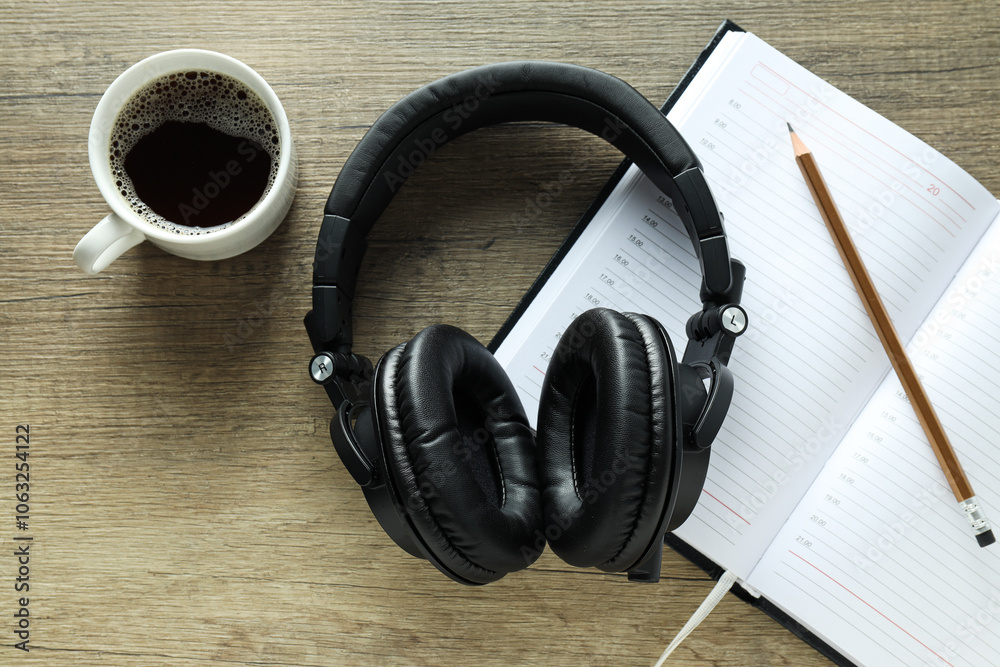 Black big headphones, on a table with a notebook and coffee. Black big headphones, on a table with a notebook and coffee.