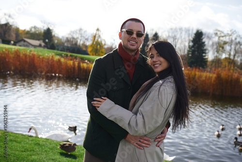 A couple in stylish autumn attire joyfully poses together by a peaceful lake, enjoying the moment. photo