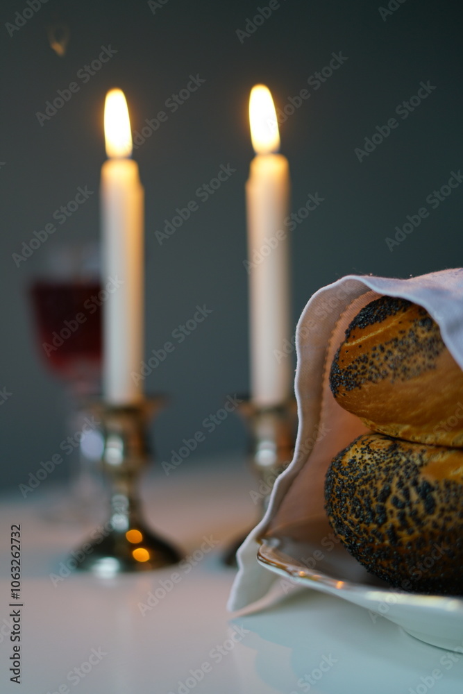 Fototapeta premium vertical photo Shabbat or Sabbath kiddush ceremony composition with a traditional sweet fresh loaf of challah bread, glass of red kosher wine and candles on a vintage wood table with copy space