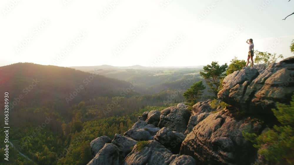 Hiker standing confidently on the rocky cliff edge, looking at the sprawling landscape in the early morning light