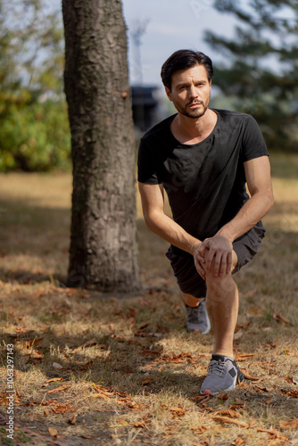 on the street in the park in the city center handsome guy brunette in black shorts and black T-shirt on the morning warm-up before jogging healthy lifestyle