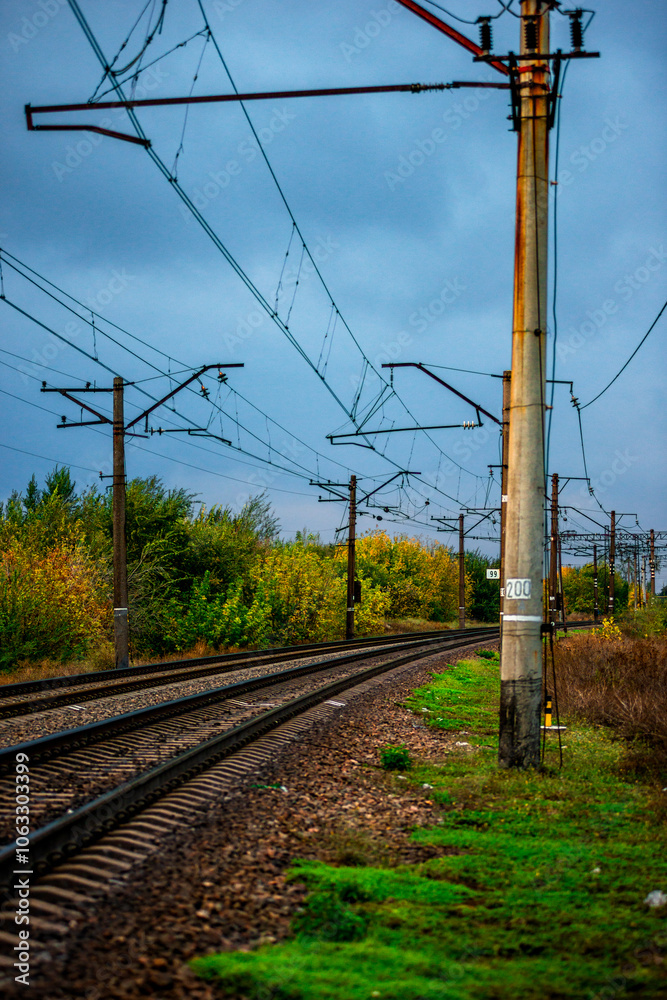 Railway road at autumn evening with autumn colors.Railroad near the forest with powerlines over the trees.Clouds in the sky,photography in the rainy weather .Landscape photo with train on the rails Railway road at autumn evening with autumn colors.Railroad near the forest with powerlines over the trees.Clouds in the sky,photography in the rainy weather .Landscape photo with train on the rails