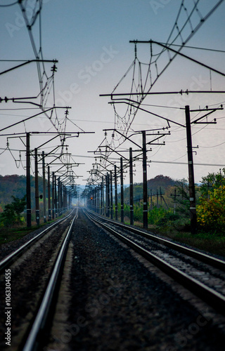 Railway road at autumn evening with autumn colors.Railroad near the forest with powerlines over the trees.Clouds in the sky,photography in the rainy weather .Landscape photo with train on the rails