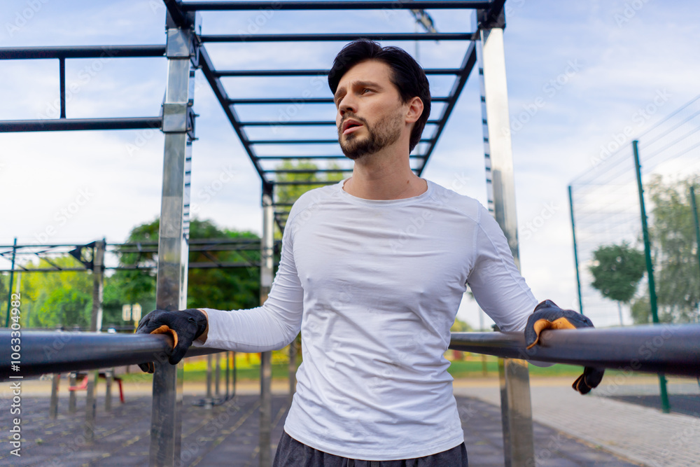 Fototapeta premium on street in the park near the horizontal bars a handsome guy brunette in black shorts and a white T-shirt doing push-ups on the horizontal bar healthy lifestyle pumping up muscles
