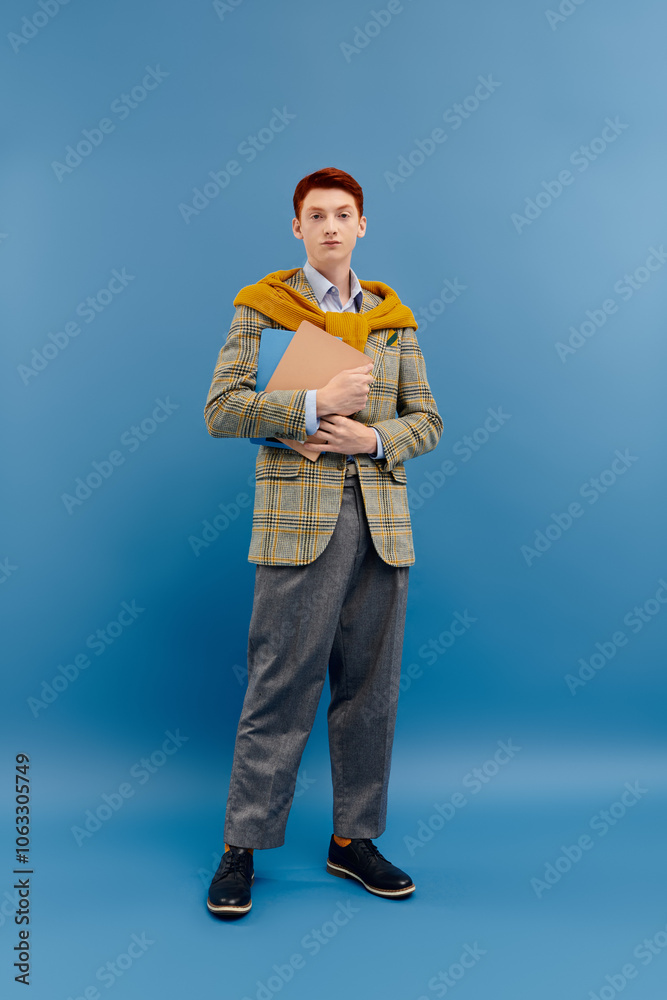 A young man with striking red hair stands confidently in a stylish winter outfit while holding a folder. A young man with striking red hair stands confidently in a stylish winter outfit while holding a folder.