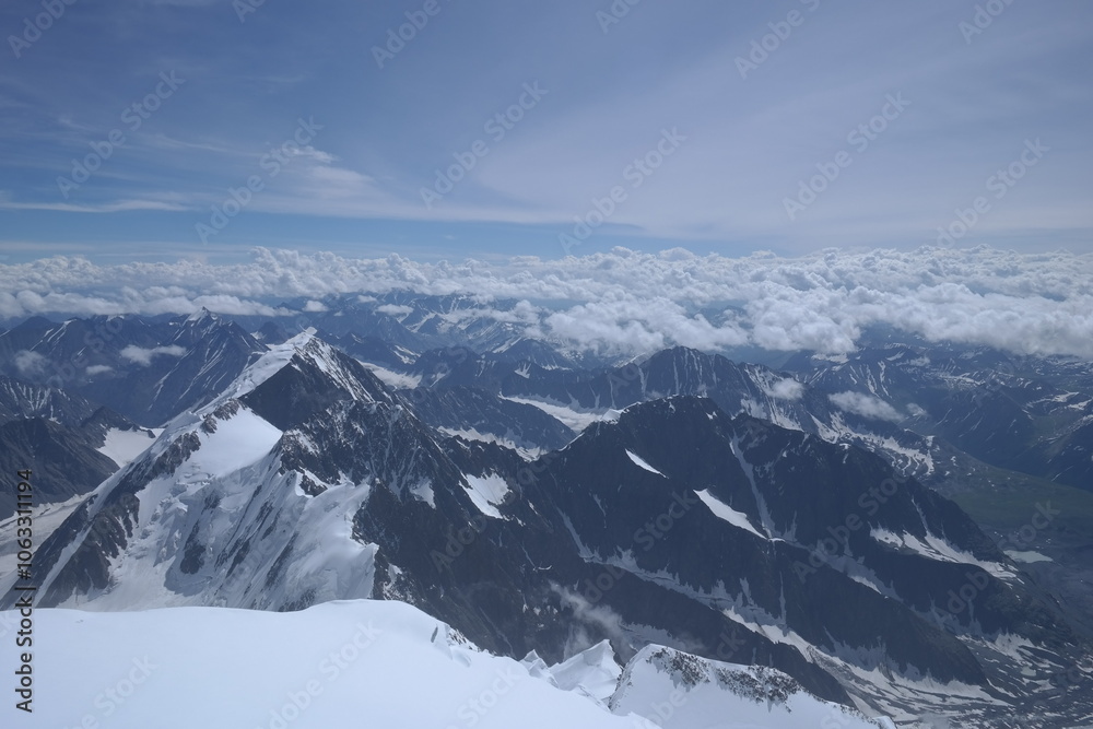 Fototapeta premium A stunning rock formation covered in snow, set against a clear blue sky with fluffy clouds in the background, creating a peaceful and breathtaking mountain landscape.