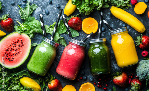 The image shows four jars of smoothies, each in a different color, surrounded by fresh fruits like bananas, strawberries, and watermelon, offering a refreshing and healthy beverage. photo