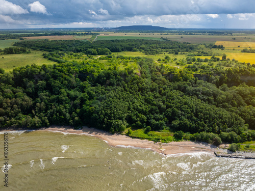 Aerial view of calm and wild Saka beach with a clear yellow water on a cloudy summer day. Beautiful yellow and green fields and countryside road. Saka, Ida Viru county, Estonia.  photo