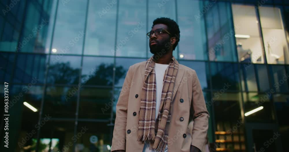 Attractive African American male walking in front of camera. Looking around while exploring new city. Tourist planning his day. Business center with glass walls in background. Lights shining. Attractive African American male walking in front of camera. Looking around while exploring new city. Tourist planning his day. Business center with glass walls in background. Lights shining.