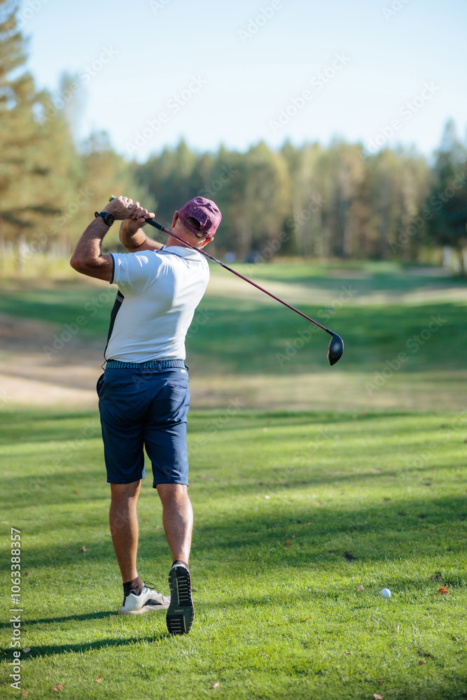 A golfer swings his driver on a sunny day at a lush green golf course A golfer swings his driver on a sunny day at a lush green golf course