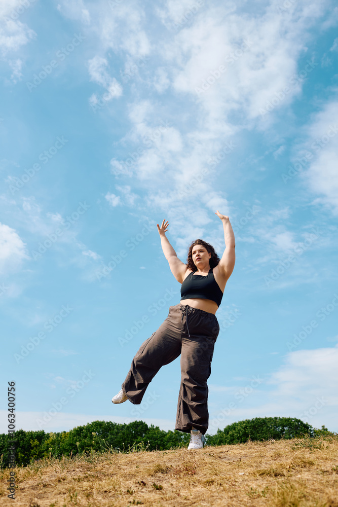 A joyful plus size woman dances freely in a vibrant field under a bright blue sky. A joyful plus size woman dances freely in a vibrant field under a bright blue sky.