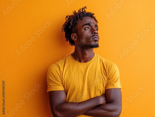 A man stands against a vivid orange background, arms crossed, looking upwards with a thoughtful expression. The image conveys a contemplative mood.