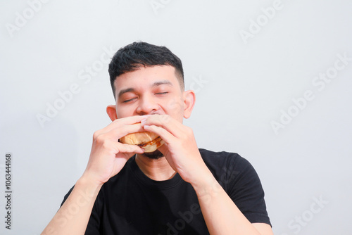 portrait of a young asian man is eating hamburger, isolated on white background. Fast food advertising