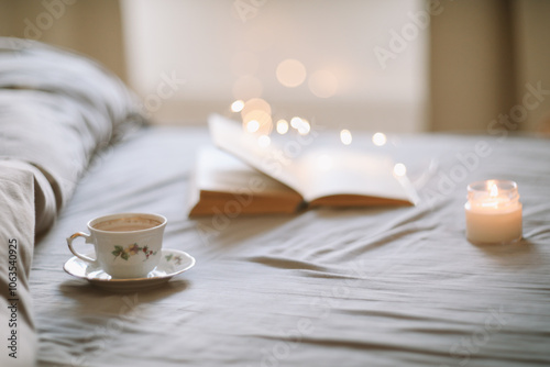 A cup of coffee and a book lying on the bed in a white bedroom