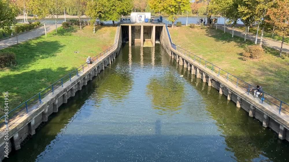 concrete dam with water canal in a park, people fishing concrete dam with water canal in a park, people fishing