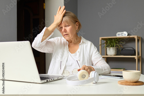 Displeased, disappointed mature woman with facepalm expression feeling regret while using her laptop at home experiencing sorrow over failed project in her freelance work photo