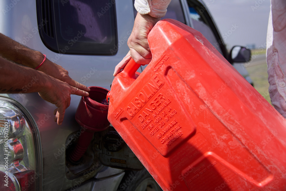 Close up view of two unrecognizable people loading gasoline into an suv from a red plastic container in a remote area. Close up view of two unrecognizable people loading gasoline into an suv from a red plastic container in a remote area.