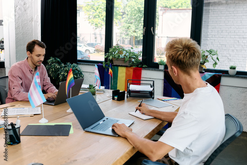 A couple collaborates passionately at a stylish table, surrounded by pride flags and greenery.