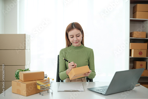 A woman is sitting at a desk with a laptop and a stack of cardboard boxes