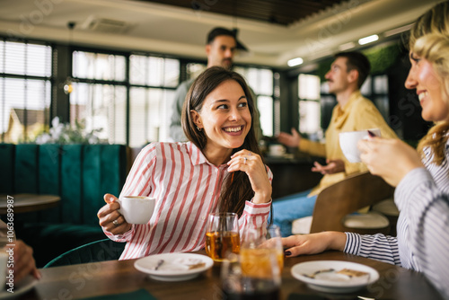 Group of female friends drinking coffee at the restaurant while the guys in the back try to flirt and send them drinks. Girl giggle and gossip about them. photo