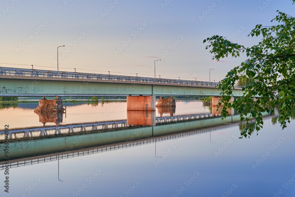 bridge spans a calm river at sunset. The sky is painted in soft hues, reflecting in the water. bridge spans a calm river at sunset. The sky is painted in soft hues, reflecting in the water.