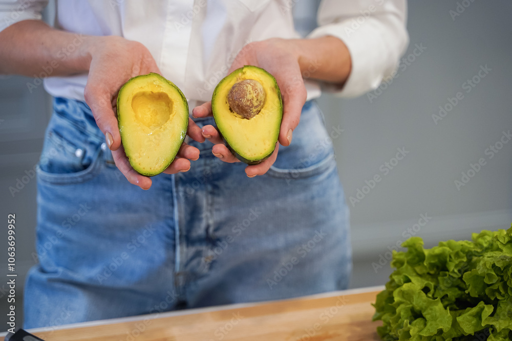 Close up of two halves of avocado in hands of female on a kitchen