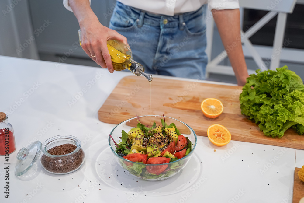 Bottle of healthy virgin olive oil pouring to salad bowl, close up