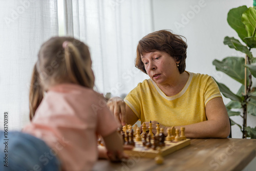 A cheerful girl plays chess with her grandmother at the table, creating precious family memories