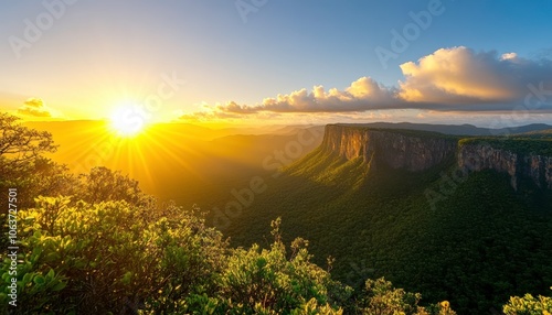 A breathtaking sunrise illuminates a lush green valley and rugged mountains, enveloping the landscape in warm golden hues. photo