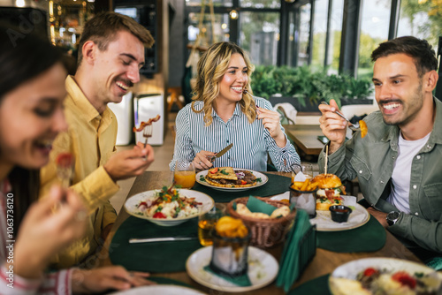 Group of happy friends eating lunch together in a restaurant. They eat delicious salads, hamburgers, bread and meat.