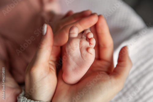 Close up mother gently holding and stroking newborn baby tiny foot in hands. Heartwarming moment, tenderness and care between mother and child, new life in soft, natural light