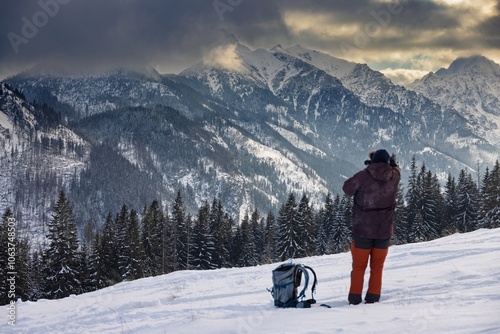 A man takes a photo of snow-covered mountains.