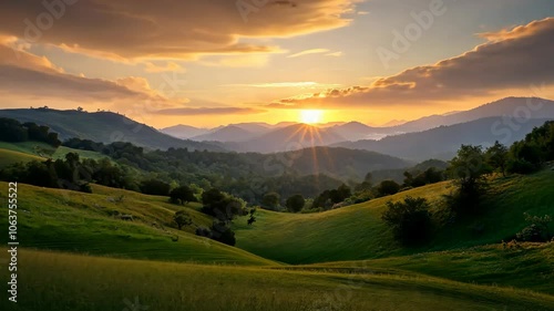 The sun sets over a rolling landscape of green hills and forested mountains