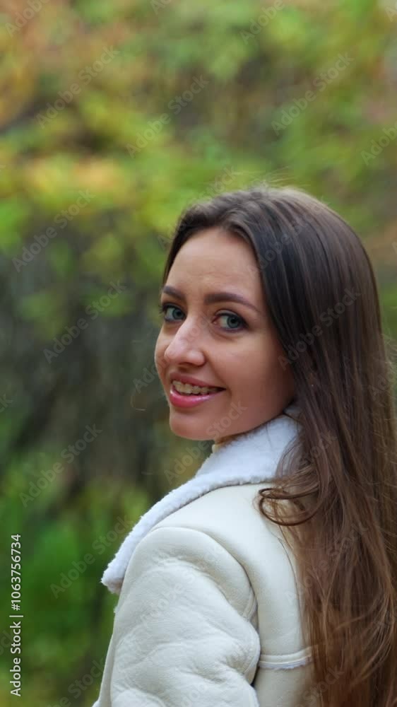 Smiling brunette in light warm jacket walking in the nature. Girl taking a stroll in the park in autumn. Blurred backdrop. Vertical video Smiling brunette in light warm jacket walking in the nature. Girl taking a stroll in the park in autumn. Blurred backdrop. Vertical video
