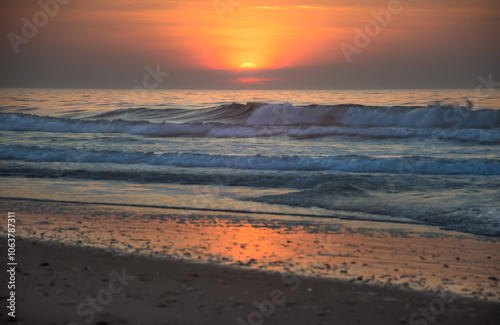 Colorful, early morning sunrise over the Atlantic Ocean, North Myrtle Beach, SC, with breaking waves and sun reflecting on sandy beach.