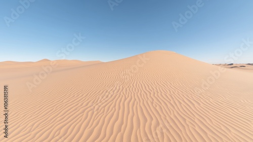 A vast expanse of rippled sand dunes stretches out under a clear blue sky in a desert landscape.