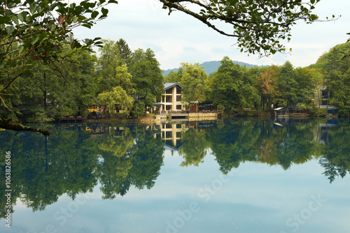 A delightful deep mountain lake of karst origin with buildings on the shore. The water with fallen leaves picturesquely reflects the trees. A natural attraction. photo