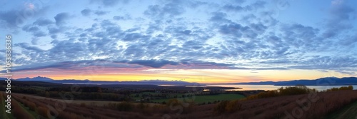 A serene landscape of rolling hills and a tranquil lake reflecting the colors of sunset, trees, dusk