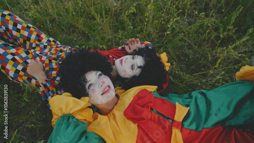 Two clowns lying in the grass in a field.