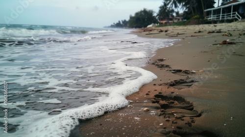 Gentle waves kiss the shore beside footprints trailing along the water, creating a serene beachscape under the soft light of an overcast day. photo