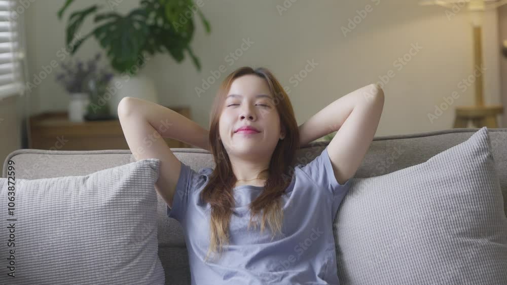 Peaceful young woman sitting on couch hold hands over head relaxing at home Peaceful young woman sitting on couch hold hands over head relaxing at home