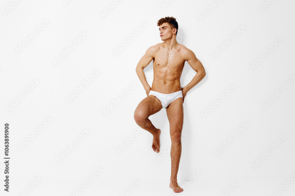 Athletic young man posing confidently against a plain white background, showcasing a fit physique in minimal swimwear. Fitness and body confidence concept. Athletic young man posing confidently against a plain white background, showcasing a fit physique in minimal swimwear. Fitness and body confidence concept.