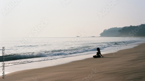 A figure at the beach reflects quietly by the shore, the gentle waves calming under the soft, expansive sky. photo