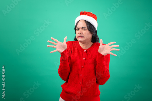 An Asian woman in a red sweater and Santa hat, with a green background, makes a disgusted face with her hands spread out in front of her, as if recoiling. She displays a humorous