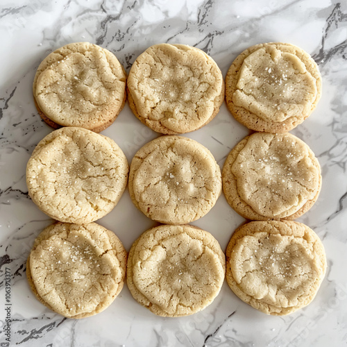 Nine freshly baked sugar cookies rest on a marble countertop, awaiting their final touch of frosting photo